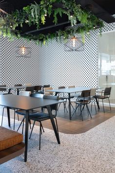 an empty table and chairs in a room with plants hanging from the ceiling above it