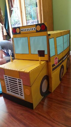 a cardboard school bus sitting on top of a hard wood floor next to a window