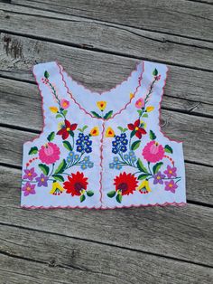 a white top with colorful flowers on it sitting on a wooden table next to a pair of scissors