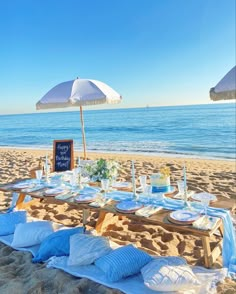 a table set up on the beach with an umbrella over it and plates laid out