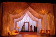 a stage set up for a wedding with gold drapes and white curtained walls