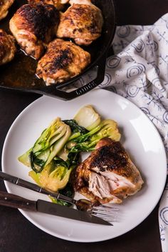 a white plate topped with meat and veggies next to a cast iron skillet