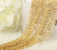 gold plated chain necklaces are displayed on a white furnishing with flowers in the background