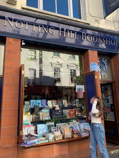 a woman standing in front of a book shop looking up at the sign for notting hill bookshop