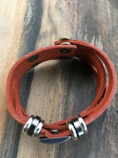 a red leather bracelet with two metal rings on top of wooden planked flooring