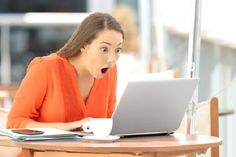 a woman sitting at a table with a laptop in front of her and looking surprised