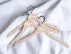 three wooden clothes hangers with personalized names and pearls on them, sitting on a white sheet