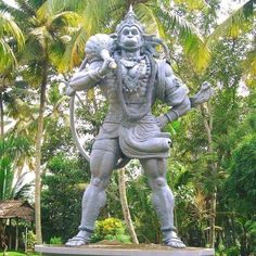 a statue of a man holding a bow in front of some palm trees and bushes