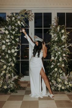 a woman in a white dress and hat standing next to a flower covered wall with flowers