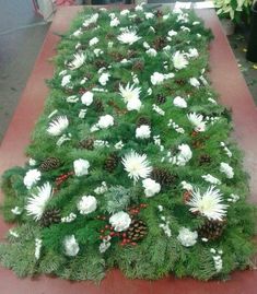 an arrangement of white flowers and pine cones on a long red table with other plants