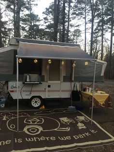 an rv is parked in the woods with its awning open and lights on above it