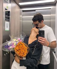 a man taking a photo of a woman with flowers on her cell phone in an elevator