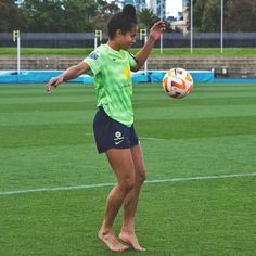 a woman is playing with a soccer ball on the field in front of some buildings