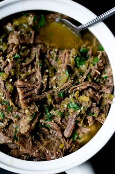 a white bowl filled with meat and green vegetables on top of a black tablecloth