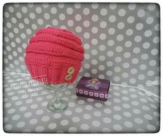 a pink knitted hat next to a small box on a polka dot tablecloth