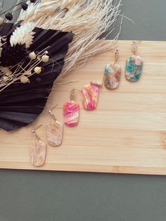 three pairs of earrings sitting on top of a wooden board next to dry grass and dried flowers