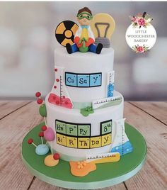 a birthday cake with science themed decorations on the top and bottom tier, sitting on a wooden table