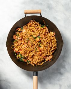 pasta with shrimp and spinach in a wok on top of a white table