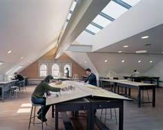 people are sitting at tables in an open room with skylights on the ceiling and windows above them