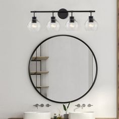 a bathroom with two sinks and a round mirror on the wall above it, along with three lights