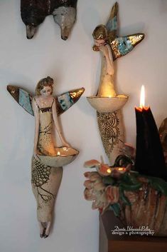 three angel figurines are hanging on the wall next to candles and other decorations