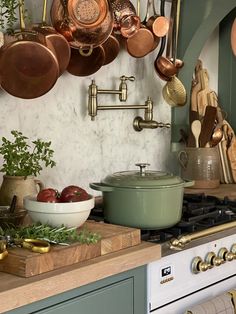 pots and pans are hanging on the wall above an oven in a kitchen with green cabinets