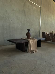 a vase sitting on top of a wooden table next to a bench with a cloth draped over it