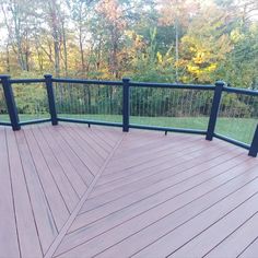 a wooden deck with black railings in front of trees