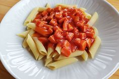 pasta with tomato sauce in a white bowl on top of a wooden table, ready to be eaten