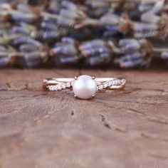 a pearl and diamond ring sitting on top of a piece of wood with lavender flowers in the background