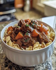 a white bowl filled with beef and pasta on top of a counter next to a stove