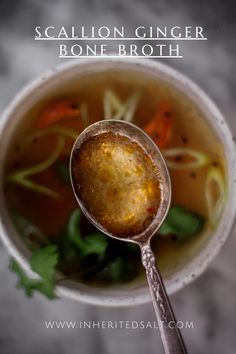 a close up of a spoon in a cup filled with soup and veggies