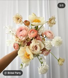 a bouquet of flowers is being held by a woman's hand in front of a white curtain