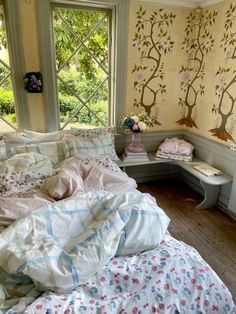 a room with a bed, desk and window that has trees on the wall behind it