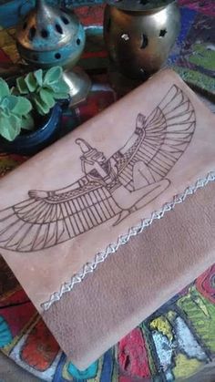 an egyptian style leather book on top of a table with some potted plants and vases