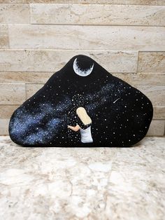 a black rock with a painting of a girl reaching for the moon