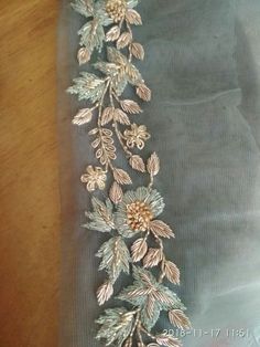 a piece of cloth with flowers and leaves embroidered on it, sitting on a wooden table