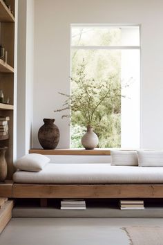 a white couch sitting in front of a window next to a wooden shelf filled with vases