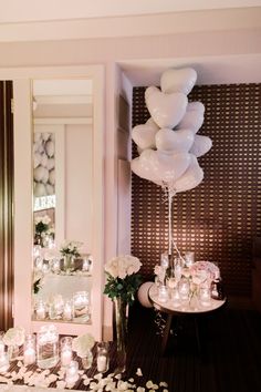 a room filled with lots of white balloons and flowers next to a table full of candles