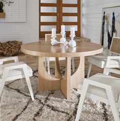 a dining room table with white chairs and a rug on the floor in front of it