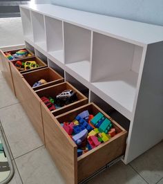 toy storage drawers with toys in them on the floor next to a wall mounted shelf