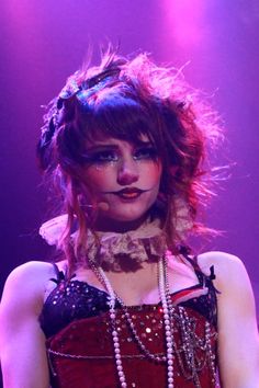 a woman with makeup on her face and pearls around her neck, standing in front of a purple background