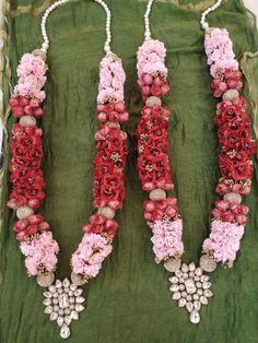 three necklaces with flowers and pearls hanging from the side on a green velvet bag