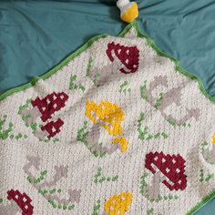 a crocheted blanket with flowers and leaves on it, laying on a bed