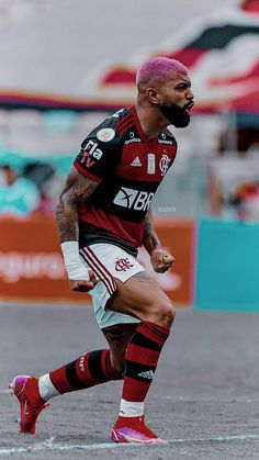 a soccer player with pink hair and tattoos on his face is running towards the ball