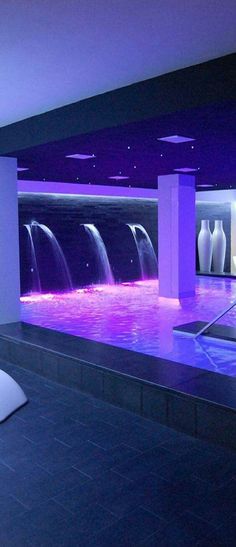 a large room with water features in the center and purple lighting on the walls, along with two white vases