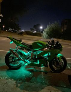 a green motorcycle is parked on the side of the road at night with its lights on