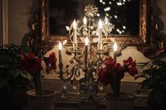 a chandelier with lit candles and flowers in front of a mirror on the wall