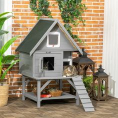 a cat house with two cats in it next to a brick wall and potted plant