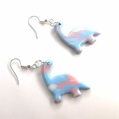 two blue and pink dinosaur shaped earrings on white surface with silver earwires hanging from them